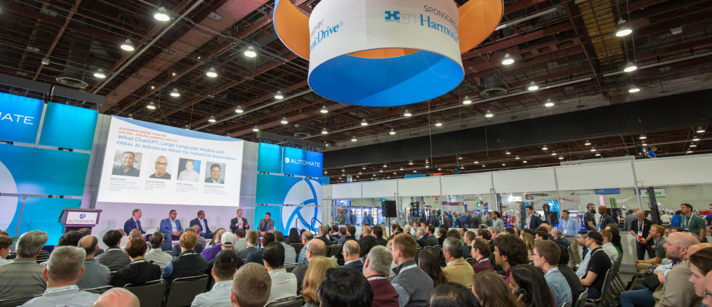 Packed Automate Show Theater panel discussion in progress, featuring a large presentation screen and audience seated in rows with overhead lighting.