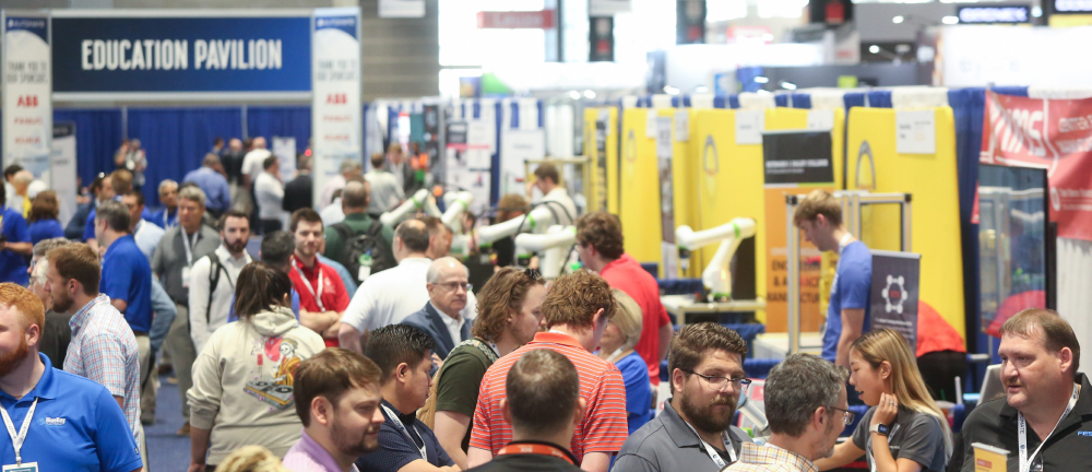  Crowded Automate Show floor with attendees networking and walking between exhibitor booths.