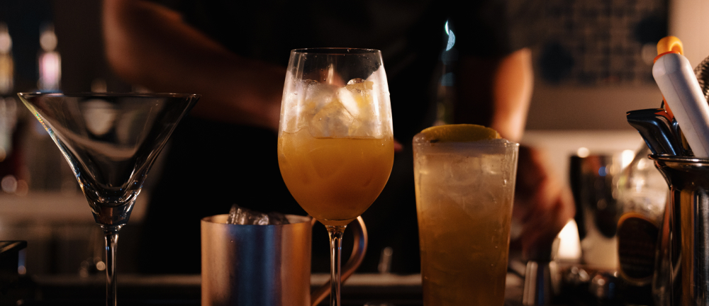 Banner image of a row of mixed drinks lined up on the bar, ready to be served to guests.
