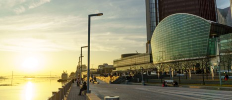 Detroit Riverwalk at sunset with the Renaissance Center in the background and golden sunlight reflecting off the river.