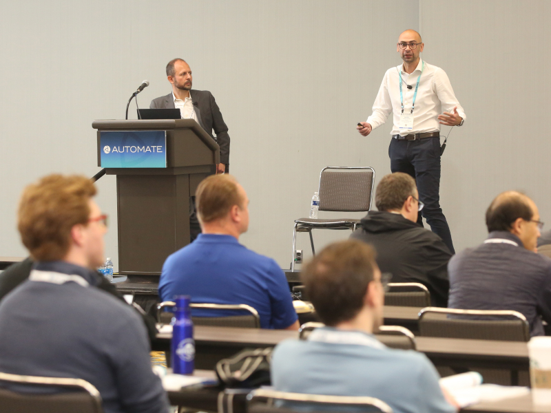 Two men speak to a classroom at Automate Show. Decorative Image.